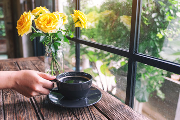 Closeup image of a hand holding a cup of hot coffee on wooden table