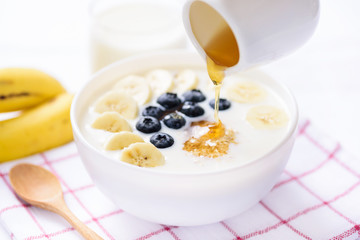 Pouring honey on oatmeal with banana and blueberry in a bowl, healthy breakfast