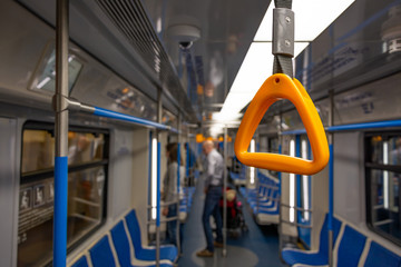 A yellow hand grip over background of an almost empty subway train, passengers with a baby stroller ready to drop off.