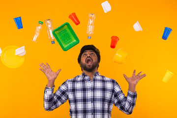 Plastic recycling problem, ecology and environmental disaster concept - Scared Indian man screaming on yellow background with trash. He is worried about ecology disaster