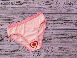 Fashionable pink women's panties with red heart on pink wooden background. Flat lay.
