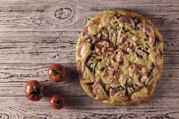 Toned image of pizza and three tomatoes on a wooden table. The view from the top.