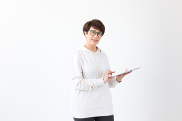 Cute middle-aged woman in casual clothes is looking online stores using a tablet on a white background. Concept of wireless internet and online shopping. Copyspace.