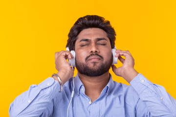 Indian man enjoy the music in his headphones on yellow background.