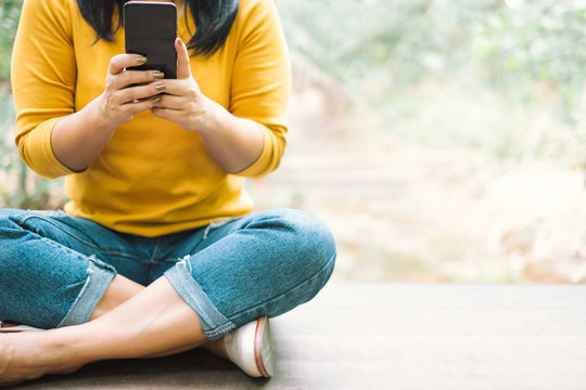 Woman In Yellow Shirt Holding A Black Mobile Phone Against Nature Background