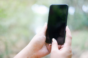 hand holding and using a mobile phone with white blank screen against bokeh of nature background