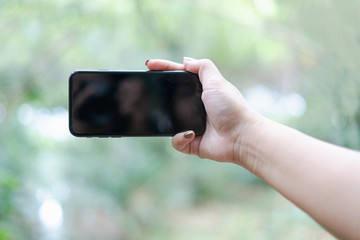 hand holding and using a mobile phone with white blank screen against bokeh of nature background
