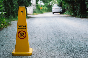 yellow no parking sign on the road against car in background