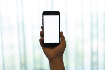 hand using a mobile phone with white blank screen against white curtain background