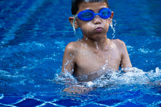 close up face of boy when comming up from diving in swimming pool and blue refreshing water.