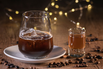 Tequila Shot's next to a cocktail served with ice, roasted coffee seeds all around and small lights on a wooden table