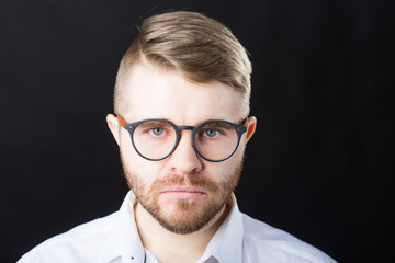 Close up portrait of handsome bearded man in stylish glasses standing against black wall