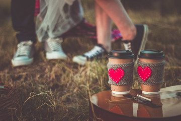 Romantic couple hugging while having picnic in sunset light. Coffee cup cozy knitted sleeve with felt red heart.