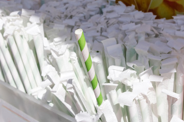 A striped green and white straw sticks out of a container of wrapped paper straws