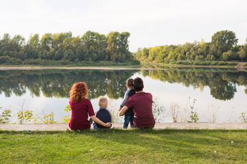 Parenthood, nature, people concept - family with two sons sitting near the lake