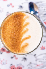 A wave pattern latte art on a glass of chai latte, with a defocused spoon in the background