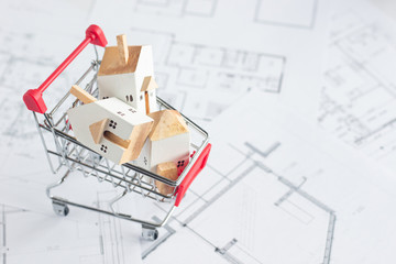 Miniature white houses decorated in red shopping cart on Architectural blueprint paper