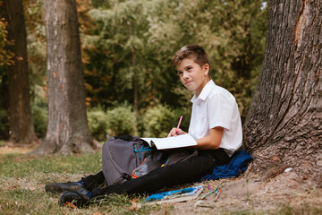 Schoolboy in a park under a tree doing homework.schoolboy sitting under a tree in the park