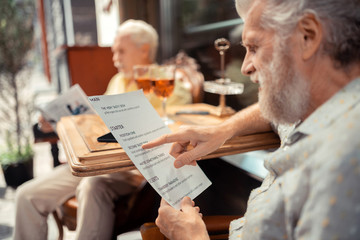 Close up of grey-haired bearded man holding menu and choosing dish