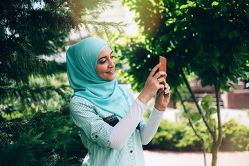 Naklejka na ściany i meble Beautiful muslim woman making selfie by smartphone at street.