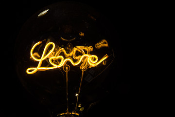 Lightbulb on dark background with bright wire in shape of the word Love