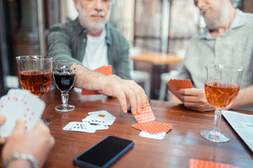 Bearded grey-haired men drinking alcohol and playing cards