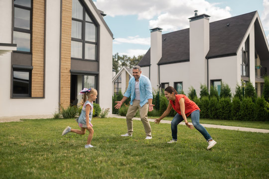 Parents And Daughter Playing Hide And Seek Outside Near House