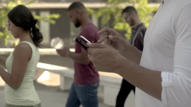 Closeup shot of male hands using tablet. Group of young people walking on street and using smartphone. Communication and technology concept