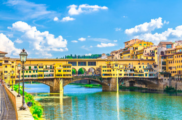 Ponte Vecchio stone bridge with colourful buildings houses over Arno River blue turquoise water and embankment promenade in historical centre of Florence city, blue sky white clouds, Tuscany, Italy