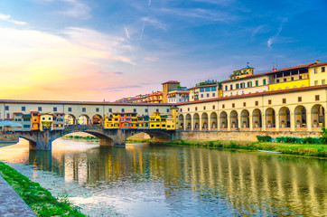 Ponte Vecchio bridge with colourful buildings houses over Arno River reflecting water and embankment promenade archways, historical centre of Florence city, blue evening sky clouds, Tuscany, Italy