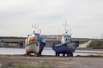 old rusty battered boats on coasters on the river bank against the background of the bridge