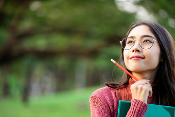 Young creative student girl thinking or planning future education while holding pencil in hand....