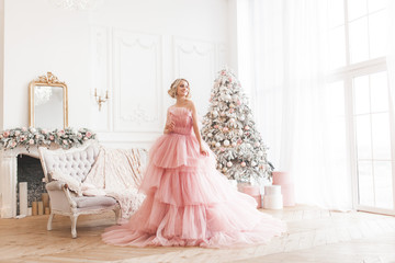 Young beautiful blond woman on christmas background full height. Attractive lady in pink gorgeous dress.