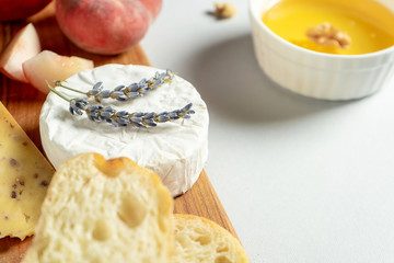 Top view different types of cheeses on wooden cutting board. Cheese with fig peach, honey, ciabatta and nuts, glass of red wine. Stylish food flat lay on grey background. Copy space. Soft focus