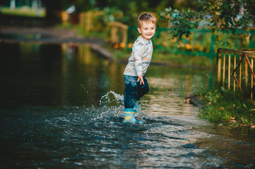 Happy child playing in puddle in rubber boots. A boy have fun after a rain.