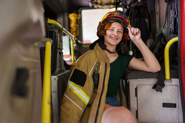 Image of happy ginger firewoman looking in camera sitting in cab of fire engine