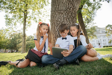 schoolchildren, two girls and a boy enthusiastically watch content on the tablet, actively commenting on what they saw.