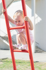 cute little blond toddler girl climbing stairs of a children's slide at playground