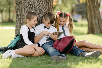 Fototapeta premium schoolchildren, two girls and a boy enthusiastically watch content on the tablet, actively commenting on what they saw.