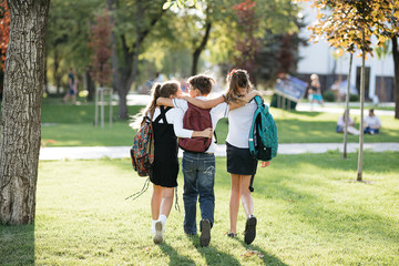 school friends a boy and two girls with school backpacks on their backs walk after class