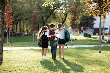 school friends a boy and two girls with school backpacks on their backs walk after class - obrazy, fototapety, plakaty