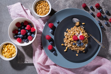 A plate of granola with raspberries and blueberries on a gray concrete background.with copy space top view