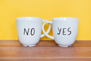Uncertainty or doubts concept, mugs with words Yes and No on the yellow background.