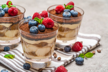 Classic tiramisu dessert with blueberries and raspberries in a glass on kitchen towel on concrete background