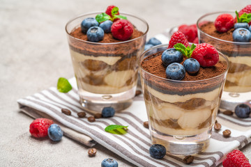 Classic tiramisu dessert with blueberries and raspberries in a glass on kitchen towel on concrete background