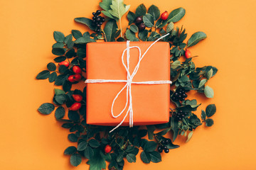 Floral decoration. Handmade gift box with rose hip berries and green leaves on orange background.