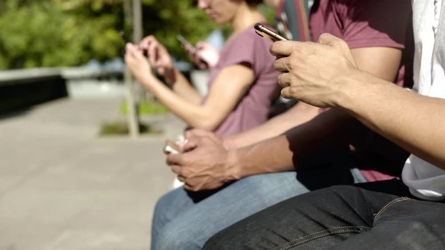 Closeup shot of people using digital devices on street. Friends sitting in row with smartphones. Technology concept
