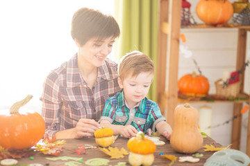 Happy halloween. Young beautiful mother and her son carving pumpkin. Happy family preparing for Halloween.