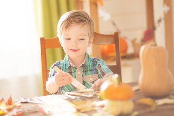 Happy Halloween concept. Cute little happy boy carving a pumpkin and decorated cookies for halloween on a table indoors.
