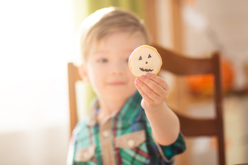 Happy Halloween concept. Cute little happy boy carving a pumpkin and decorated cookies for halloween on a table indoors.